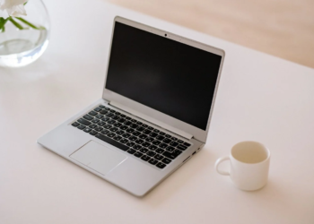 Silver laptop with screen off on white desk beside a coffee mug and flower vase
