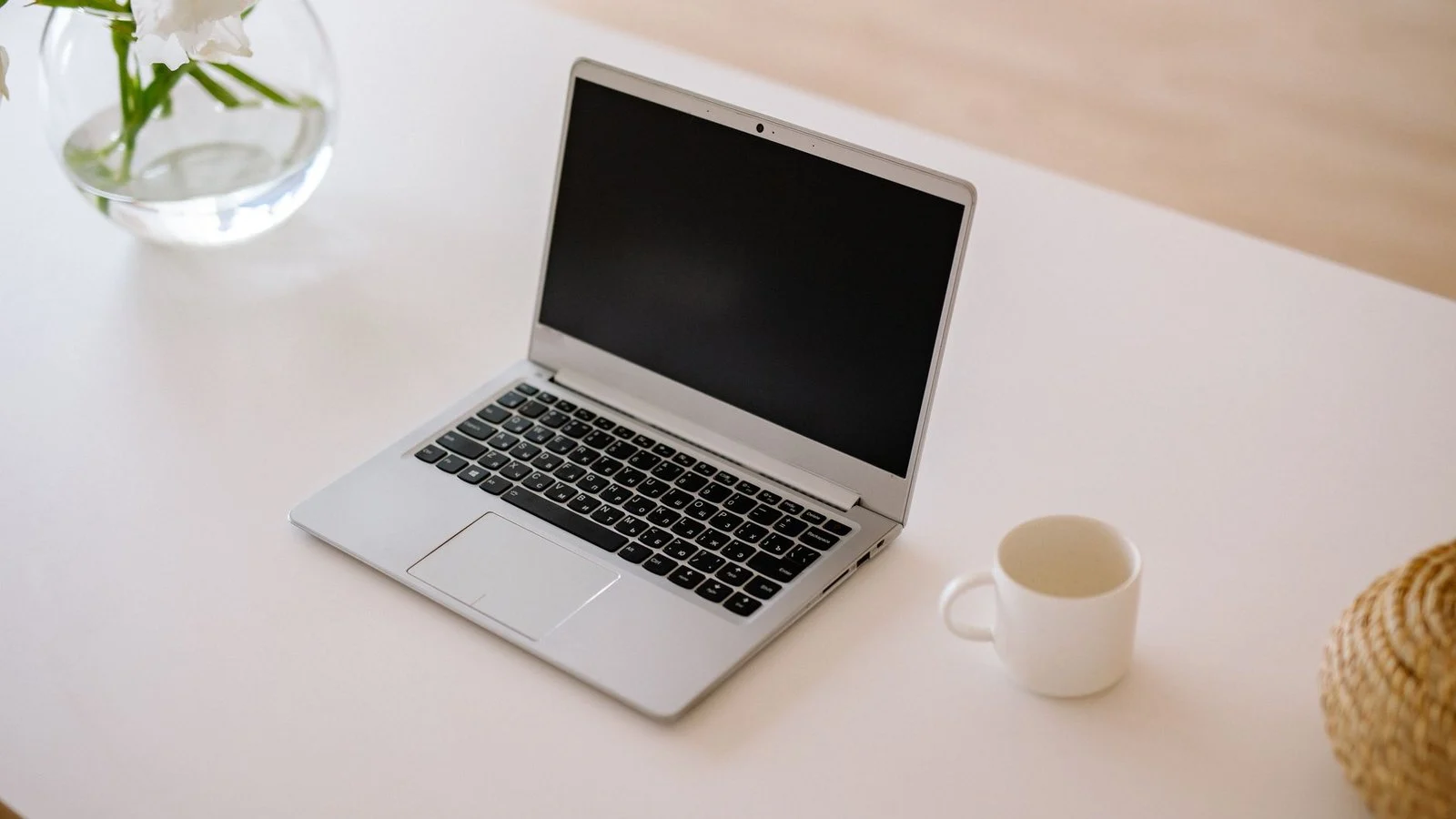 Silver laptop with screen off on white desk beside a coffee mug and flower vase
